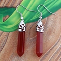 Dettaglio di orecchini di cristallo esagonale rosso con ganci d'argento incisi su legno - Agata rossa