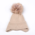 Detail showing beige ribbed knit texture and soft faux fur pompom on winter beanie hat - Beige