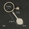 Silver metal tennis racket keychain with yellow ball pendant on textured black surface - Tennis Ball