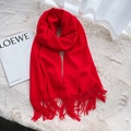 Bright red cashmere-feel scarf with long tassels laid flat on a soft plush white rug - Red