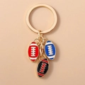 Dettaglio del portachiavi in metallo dorato con ciondoli da rugby in smalto rosso, blu e nero - 3 palloni da rugby (Multicolore)