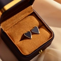 Detail van hartvormige zwarte emaille oorbellen met gouden rand in een luxe sieradendoos - Zwart