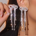 Elegant silver bow earrings with long sparkling rhinestone tassels on model ear - Stud Earrings / Silver White Rhinestone