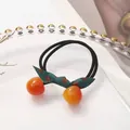 Elastic hair tie with red resin beads and a green polka dot bow on white tray - Orange Red Cherry Bow