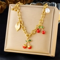 Detalle de pulsera dorada con colgante de cereza en esmalte rojo y detalles de perlas - Estilo de Colgante de Cereza Hoja Perla (N3399)