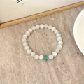Artistic white natural stone beaded bracelet with green accent bead on marble surface - White Cat's Eye with One Green Cat's Eye