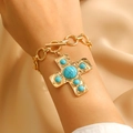 Golden chain bracelet with a turquoise-set cross charm worn by a model on beige fabric - Gold Turquoise Bracelet (X343)