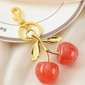 Close-up of a glittery red cherry keychain with gold metal chain on a white ceramic plate - Gold Double Leaf Pink Cherry