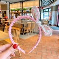 Détail d'un serre-tête floral rose avec un nœud à motif cerise tenu à la main - Rose Fleuri