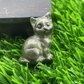Miniature natural stone cat figurine with tilted head sitting on artificial grass - Chalcopyrite