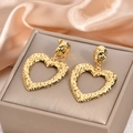Detailed close-up of hollow gold heart earrings with textured surface on silk fabric - Textured Hollow Heart Drop Earrings / 925 Silver Needle