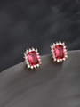Detalle macro de pendientes dorados con piedra roja de corte esmeralda y circonitas blancas - 1.1x0.9cm / Bañado en oro de 18K - Rosa roja