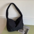 Detail view of black quilted puffer tote bag on a light green table with a magazine - Black