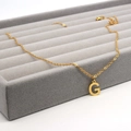 Detail of a gold stainless steel letter G pendant on a luxury velvet display tray - Letter G / Gold