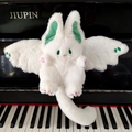 White bat bunny plush toy with green wings and ears sitting on a piano keyboard - White Rabbit
