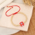 Macro view of gold beaded bracelet with a red cubic evil eye charm and red cord - Red