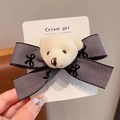 Dettaglio del fermaglio con fiocco grigio e orsetto di peluche su carta Cream Girl - Orso con fiocco / Grigio