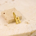 Macro detail of a minimalist gold letter H pendant on a beige natural stone base - Letter-H / Steel