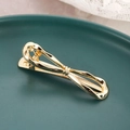 Elegante goudkleurige metalen haarclip in strikvorm op een groen keramisch bordje - Goud