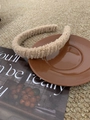 Close-up of a beige plush faux shearling headband on a brown ceramic saucer - Beige