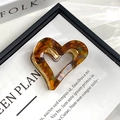 Macro detail of amber heart hair claw clip with golden trim and premium resin texture - Heart Coffee