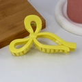 Detail view of a bright yellow ribbon-shaped hair claw clip on a white desktop surface - Glossy Yellow