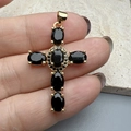 Detail shot of a gold cross pendant with oval black gemstones on a hand for scale - Black
