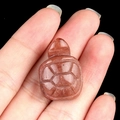 Handcarved red natural stone turtle figurine with detailed shell texture on fingertip - Purple Aventurine