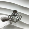 Detailed view of silver metallic scallop shell hair claw clip held by a gloved hand - Shell Style / Silver