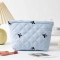 Detail of light blue quilted cosmetic bag with black ribbon embroidery in home setting - Light Blue