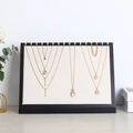 Black wooden jewelry display board with beige fabric and multiple gold pendant necklaces - Hemp Fabric