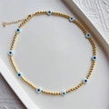 Elegant gold bead necklace with blue and white evil eye charms on a ceramic tray - Gold Round Beads with Blue White Evil Eye (JSX220008B)