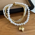 Detail of layered gold heart pendant necklace with pearls on a rustic wood background - Gold