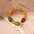 Dettaglio di un bracciale dorato con ciondoli a uovo in smalto e fiocchi di strass lucidi - Bracciale Multicolore