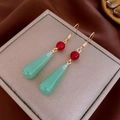Dettaglio macro di orecchini dorati vintage con perline rosse e ciondoli a goccia verdi - Stile Perla Rossa Goccia Verde