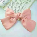 Pink oversized satin bow hair clip with spring fastener shown on a book background - Duckbill Hair Clips / Champagne Pink