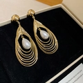 Close-up of layered gold hollow earrings with a drop pearl on black velvet - Gold