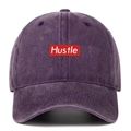 Close-up of a washed purple baseball cap featuring a red rectangle Hustle embroidery - One Size / Purple