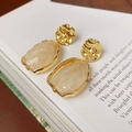 Detailed macro shot of irregular golden earrings with marble resin pendants on a book - Off-White Marble Irregular Style / Silver Earring Post-White