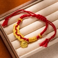 Detail of red braided bracelet featuring gold coins and Buddha pendant on a display box - L269-7 Arrival of Wealth God