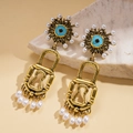 Detalle de pendientes vintage dorados en forma de candado con perlas y ojos azules - Dorado