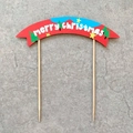 Detail view of paper Merry Christmas cake topper with red and blue banners and wooden sticks - Red And Blue Merry Christmas Banner