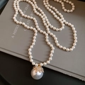 Close-up of a large white pearl pendant with a gold diamond-set crown on a book - White
