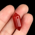 Handheld view of a polished dark red hexagonal crystal pendant with a pre-drilled hole - Red Agate