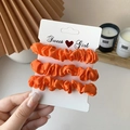 Three-piece set of vibrant orange satin scrunchies on a branded white display card - 3 Piece Set / Orange Red