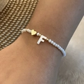Close-up of white beaded bracelet featuring a gold heart and letter F charm on wrist - Letter F