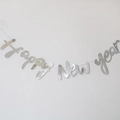 Detail of silver metallic Happy New Year banner hanging on a white wall for party decor - Cursive Happy New Year Silver