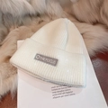 Close-up of white knitted beanie featuring a THE FOCUS embroidered label on soft plush fabric - Letter Label Style / White