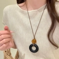 Gros plan d'un collier pendentif perle ambre et donut noir sur cordon marron - 50# Collier-Noir-Rond