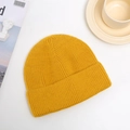 Detailed close-up of thick knitted ginger yellow beanie hat texture on a white surface - One Size / Yellow